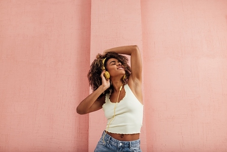 Woman with curly hair enjoying music against pink wall