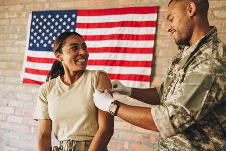 Happy servicewoman smiling at the military nurse after vaccination