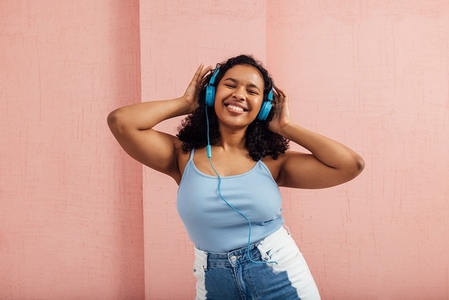 Happy woman with curly hair enjoying music listening by blue headphones