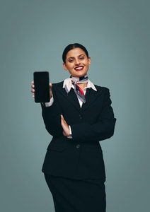 Cheerful flight attendant holding up a smartphone in a studio