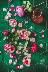 Rose lemonade with ice and rose petals over green table