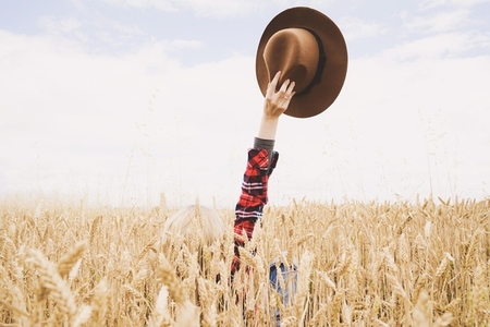 Hand holding a cowboy hat over a field of wheat