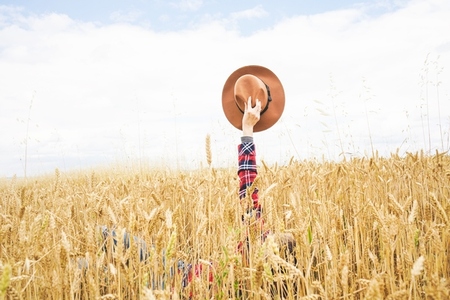 Hand holding a cowboy hat over a field of wheat