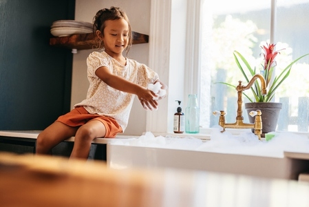 Young girl playing with soap bubbles in the kitchen