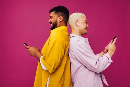 Smiling gay couple using mobile phones in a studio