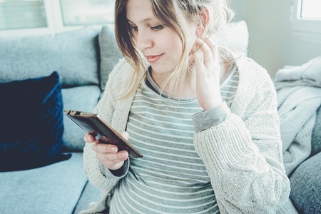 Young pregnant woman at home using her mobile phone