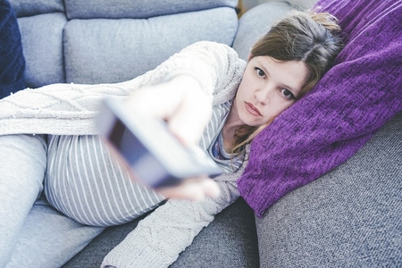 Young pregnant woman boring and watching tv at home