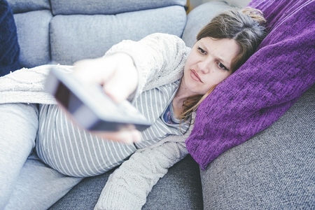 Young pregnant woman boring and watching tv at home