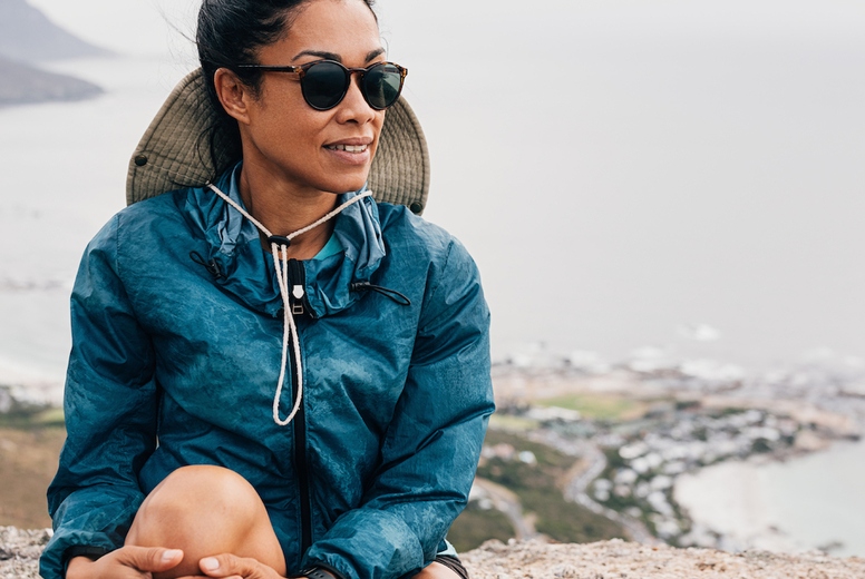 Woman relaxing during a hike. Young female wearing sunglasses sitting on a cliff.