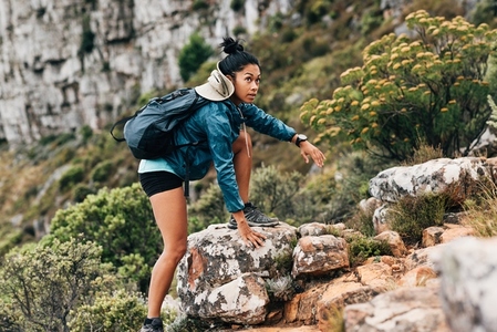Woman hiker climbing up on a rock  Young female in sports clothes with backpack hiking on mountain terrain