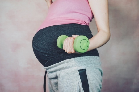 Young pregnant woman doing exercise with a dumbbell