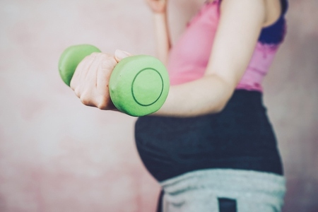 Young pregnant woman doing exercise with a dumbbell