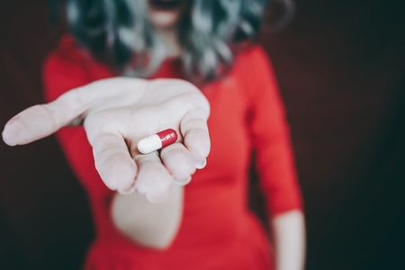 Young womans hand holding a white and red pill