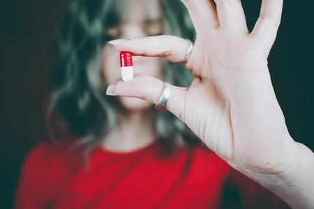 Young womans hand holding a white and red pill