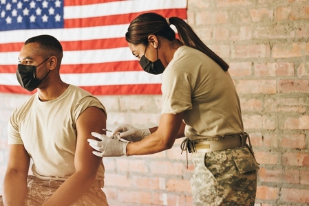 Army doctor administering the covid 19 vaccine to a soldier