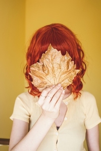 Redhead young woman covering by a dry autumn leaf