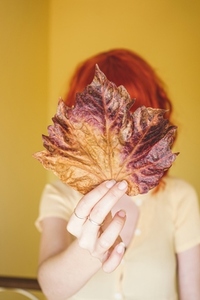 Redhead young woman covering by a dry autumn leaf
