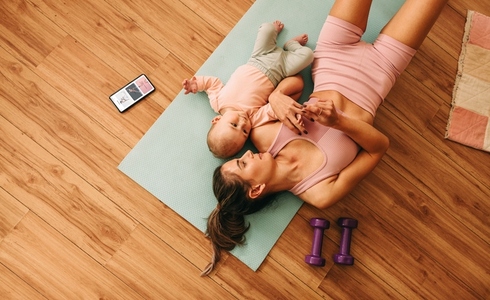 Overhead view of a mom lying on an exercise mat with her baby