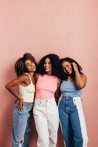 Group of three female friends leaning pink wall wearing bright casual clothes