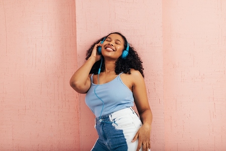 Young woman enjoying music while leaning pink wall  Female wearing blue headphones with closed eyes