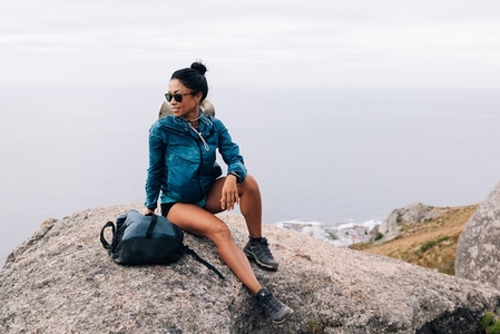 Smiling woman in sports clothes with backpack sitting on a cliff and enjoying the view