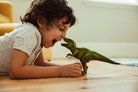 Adventurous young boy imitating a t rex dinosaur toy at home