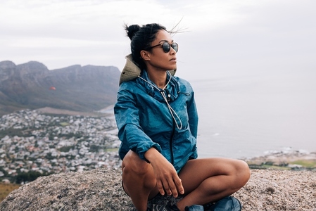 Young woman hiker relaxing and enjoying the view sitting on a cliff