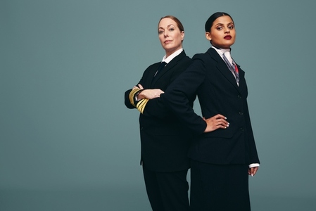 Female pilot and flight attendant standing together in a studio