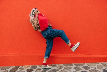 Excited senior woman dancing and having fun against a red wall
