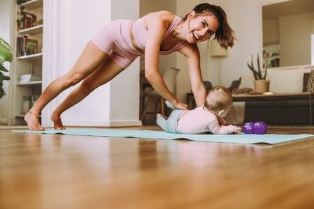 Happy young mom working out with her baby at home