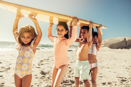 Playful little kids carrying a surfing board at the beach