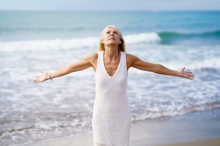 Happy mature woman opening her arms on the beach  spending her leisure time  enjoying her free time