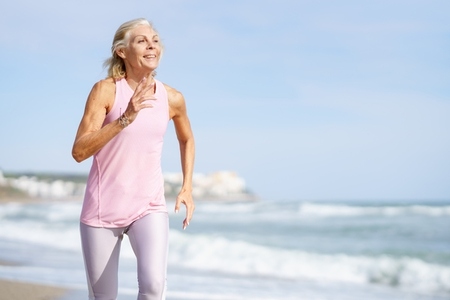 Mature woman running along the shore of the beach  Older female doing sport to keep fit