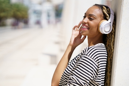 Black girl listening to music with wireless headphones outdoors