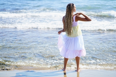 Black woman walking along the shore of the beach wearing a beautiful long dress