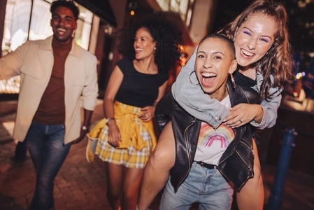 Energetic young woman piggybacking her friend outdoors at night