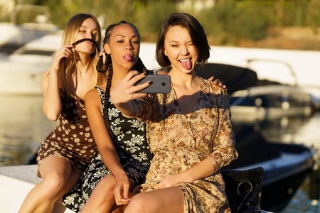 Funny multiracial women making faces while taking selfie near river