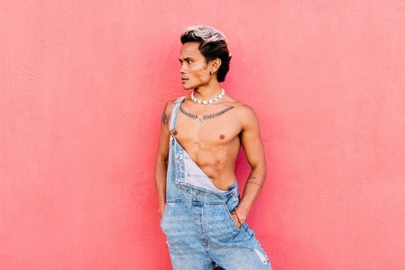 Portrait of a young handsome guy wearing overalls standing outdoors at pink wall