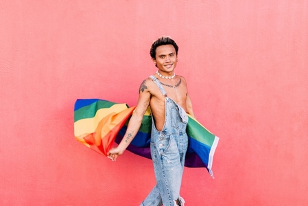 Smiling young gay man standing with pride flag  Happy guy in casuals holding LGBT flag outdoors