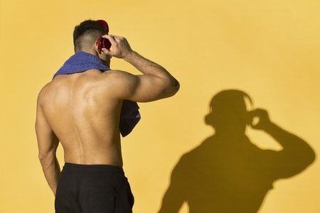 Athletic bare chested man with headphones and shadow on yellow background