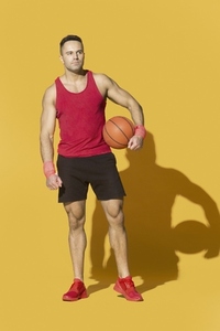 Studio portrait man in red athletic clothing with basketball on yellow background
