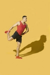 Strong athletic man with shadow stretching leg against yellow background