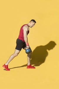 Strong athletic man with kettle bell against yellow background