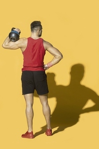 Athletic man in sportswear with kettle bell and shadow against yellow background