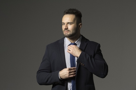 Portrait confident stylish businessman in suit adjusting tie against black background