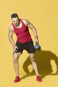 Athletic man in red sportswear lifting kettle bell against yellow background