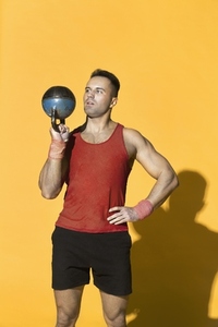 Strong athletic man lifting kettle bell against yellow background