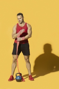 Athletic strong man with kettle bell wrapping wrist with bandage