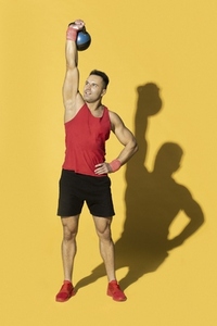 Athletic man in red sportswear lifting kettle bell overhead
