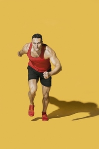 Studio portrait determined athletic man running on yellow background